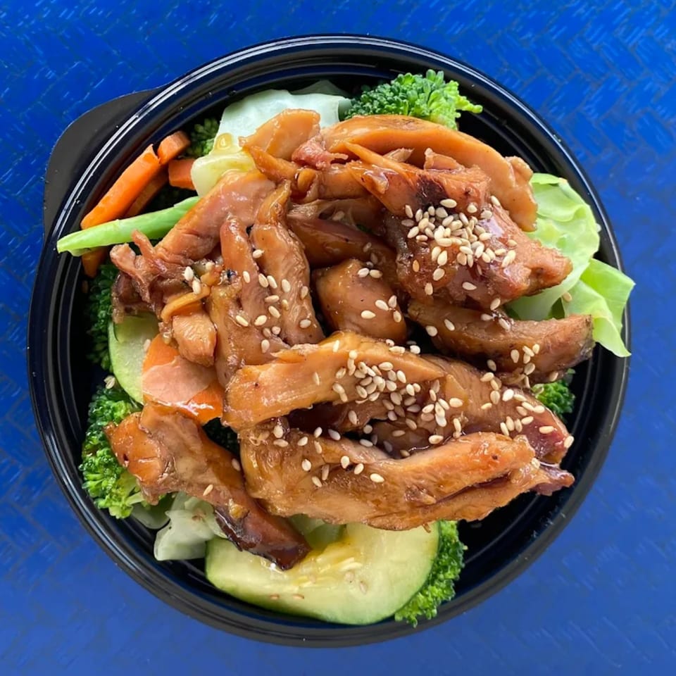 Blue Fin's chicken teriyaki bowl with broccoli, carrots, and sesame seeds on a blue background.