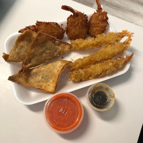 A white tray holds fried wontons, coconut shrimp, and tempura shrimp with two dipping sauces.