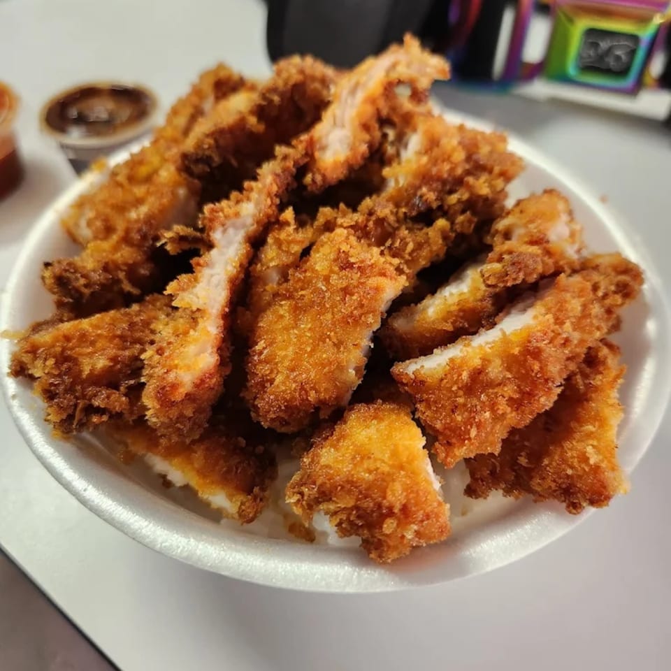 A white styrofoam plate filled with golden-brown, crispy fried chicken or pork cutlets, with dipping sauces in the background.