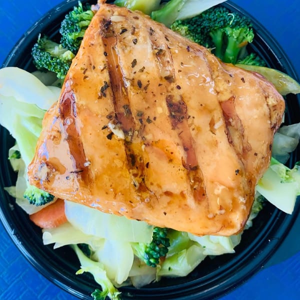 Grilled salmon with a glaze, served over broccoli and cabbage in a black bowl.