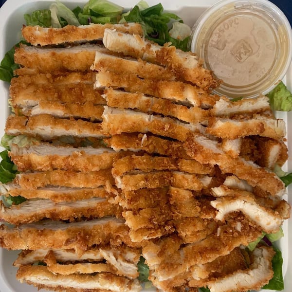 Crispy fried chicken cutlets, sliced and served over a bed of fresh green lettuce with a side of sauce.